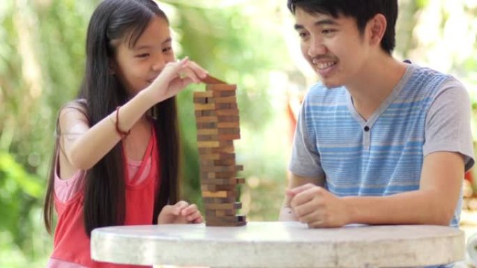 亚洲女孩玩冒险游戏，试图与父亲一起移动木块