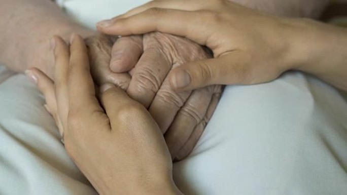 一位年轻的女性双手安慰一双老人的手