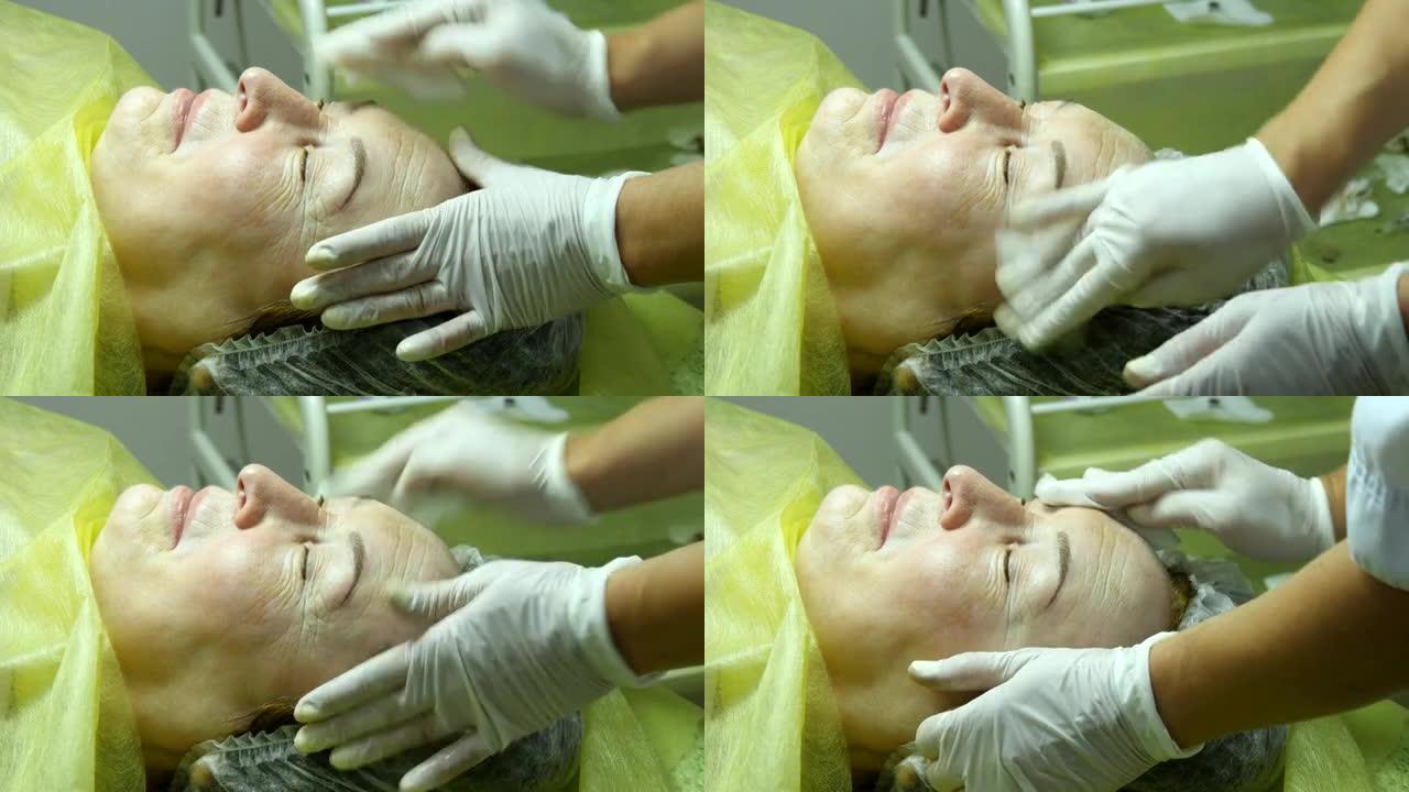 美容师的手正在为手术或手术后的清洁准备皮肤。老妇人在美容院撒谎和化妆。在睫毛上涂抹永久化妆。