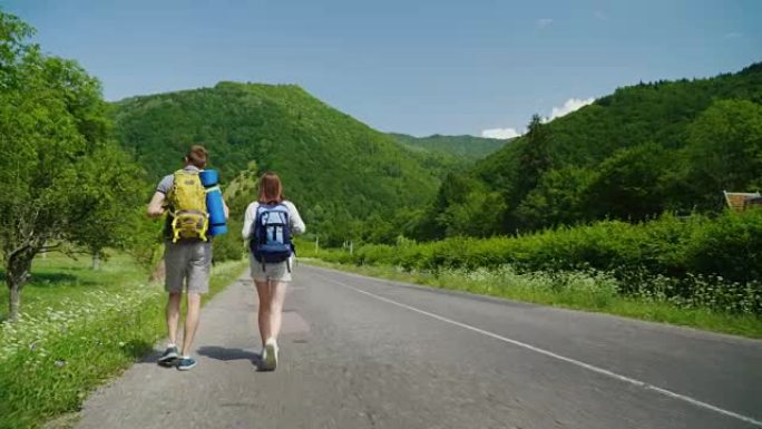 一对背着背包的游客正沿着柏油路走向美丽的青山