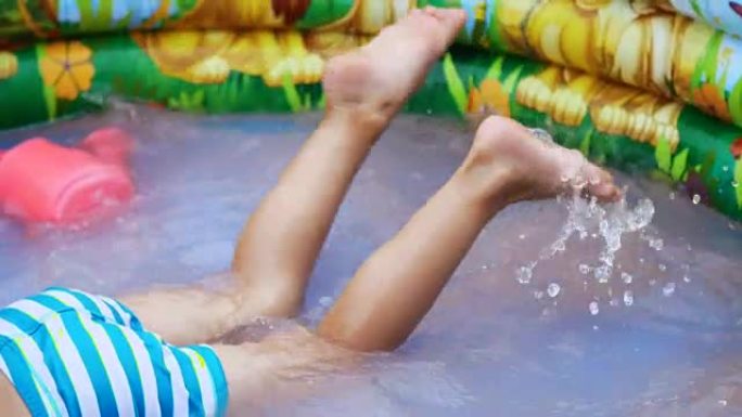 脚的特写。一个四岁的男孩躺在儿童充气池中，溅水，溅水散落。附近的漂浮玩具