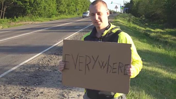 搭便车旅行的年轻成年男子到处显示在州际公路上竖起大拇指的书面标牌