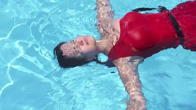 穿着红色长裙闭着眼睛的年轻女孩漂浮在游泳池里