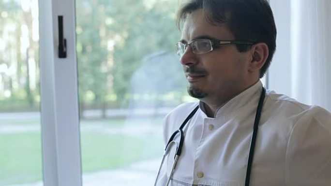 一位身穿白大褂、脖子上挂着听诊器的医生站在窗前说话。