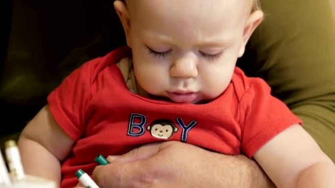 有吸引力的婴儿画与他的祖父在纸上的标记。一个男孩坐在他爷爷家里的腿上。孩子1年