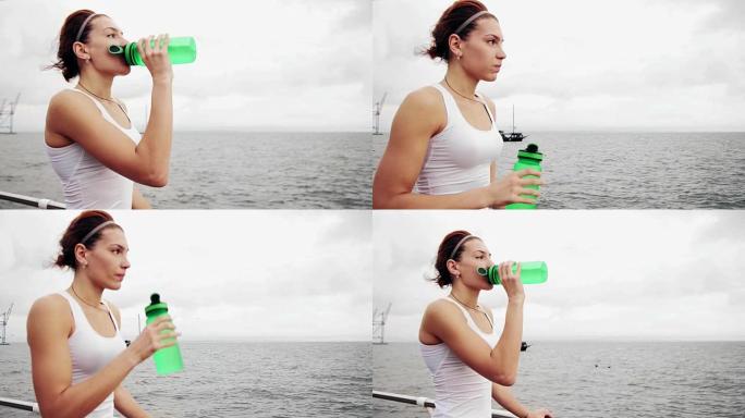 训练结束后，口渴的健身女子休息，用水瓶喝水。海边训练的美女