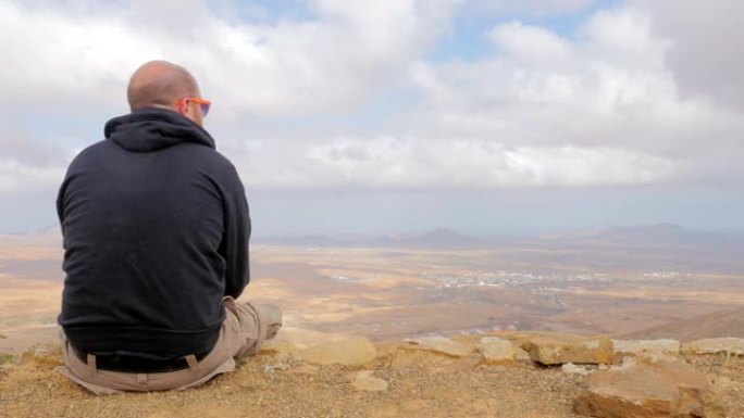 秃头男子坐在山顶上看着地平线思考他的未来