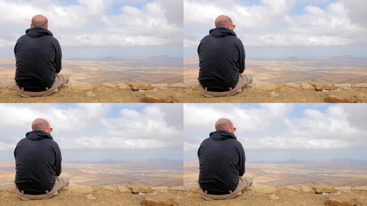 秃头男子坐在山顶上看着地平线思考他的未来