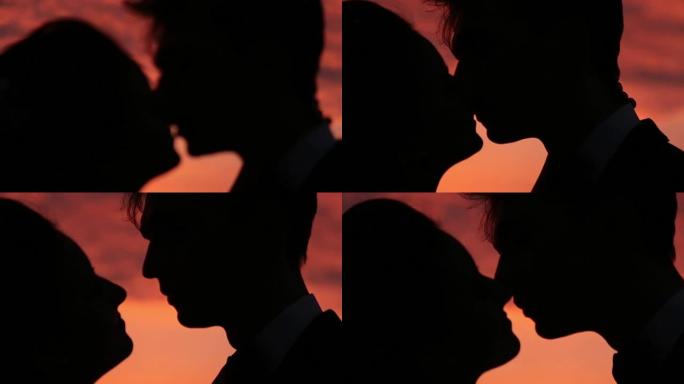 迷人的婚礼情侣在日落时接吻的剪影特写
