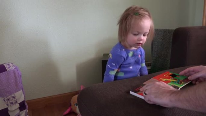 爸爸和穿着蓝色睡衣的蹒跚学步的女孩一起读书。用索尼PXW-Z100 UHD相机制作的4k视频，分辨率
