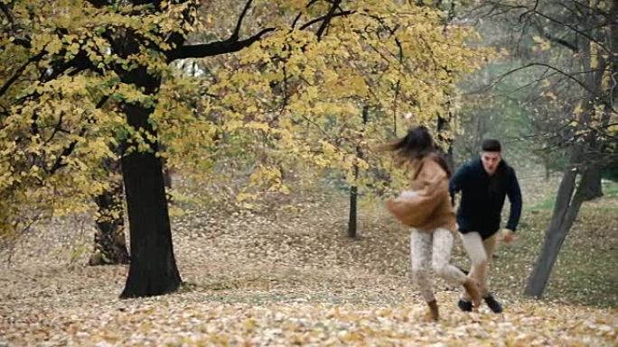 年轻顽皮的夫妇在秋天的森林里追逐时玩得很开心。慢动作。