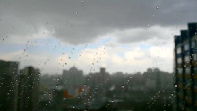 在暴风雨的日子里，雨滴的城市景观落在窗户上，俯瞰背景中的城市天际线