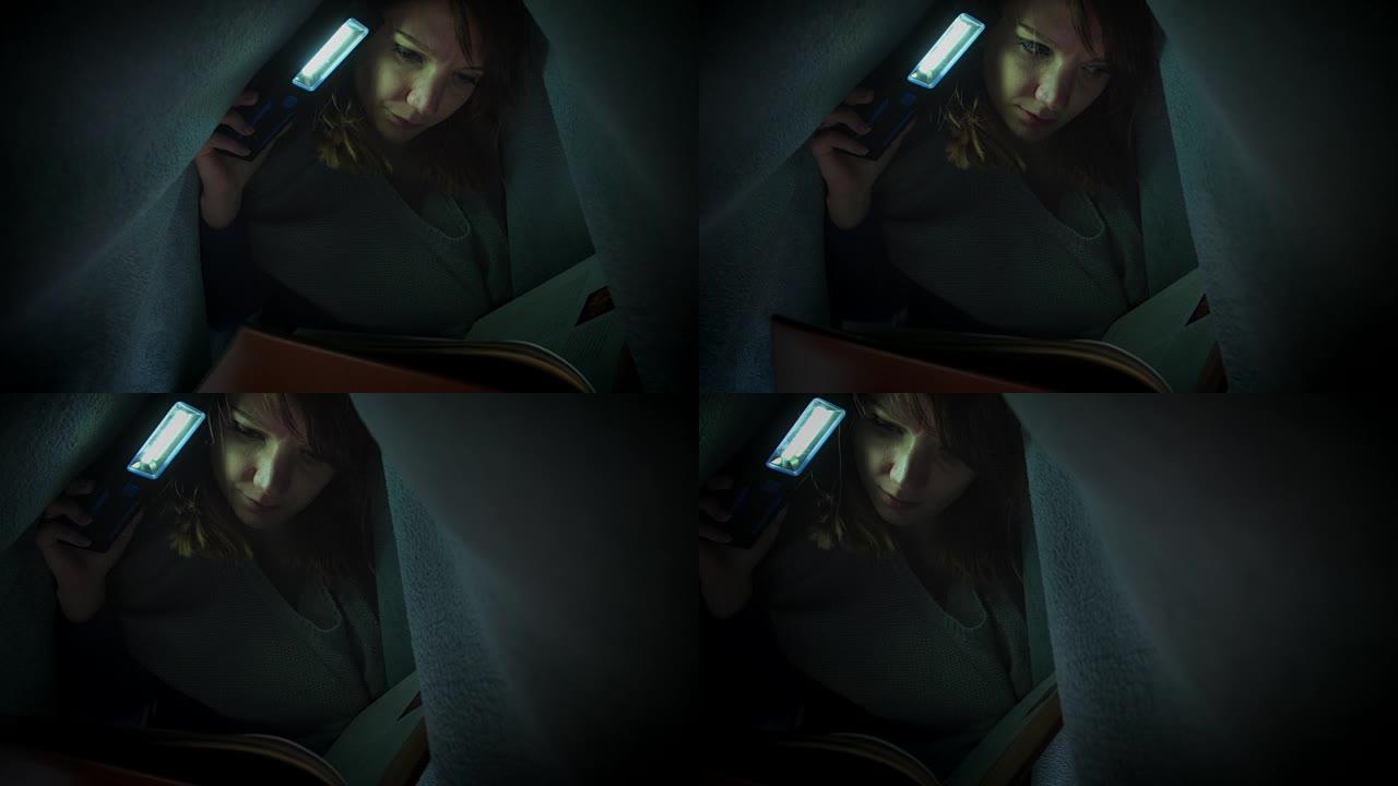 用手电筒在毯子下读书的女人的4k照片