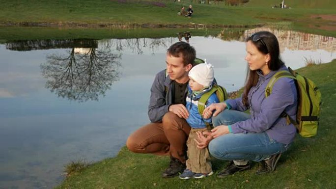 一个活跃的年轻家庭带着婴儿坐在公园的湖边，互相交谈