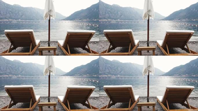 在群山环绕的海滩上，两把带太阳伞的躺椅 -- 避暑度假4k视频背景