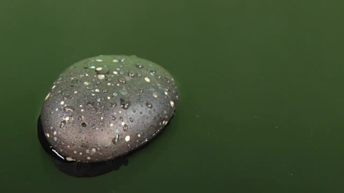 一滴水落在绿色的水和黑色的石头上