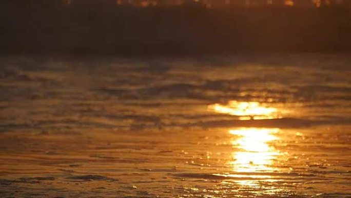 美丽的金色海浪在日落。橙色的日出倒映在海水上。在刮风的夜晚，带着波浪的潮水溅起水花。自然背景特写慢动