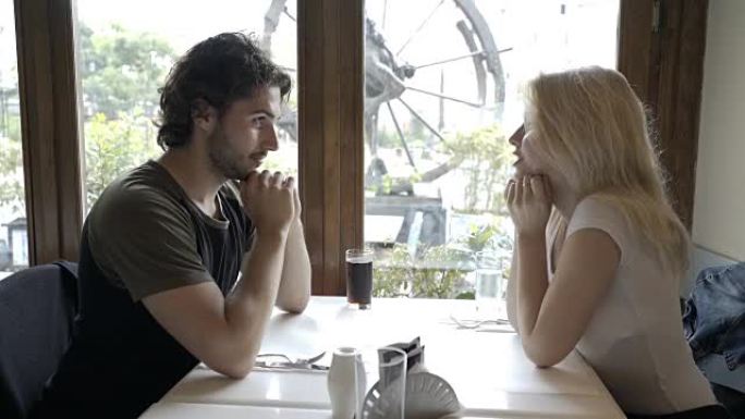 年轻人坐在酒吧里，和他迷人的女友在桌子上亲吻她的手
