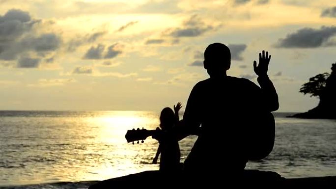 日落海滩上向年轻女士弹奏吉他的男子剪影