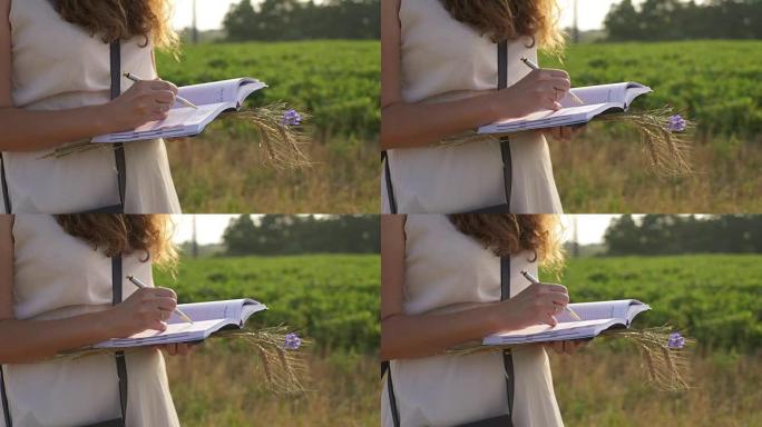 女手用笔在外面草地上的笔记本上写字