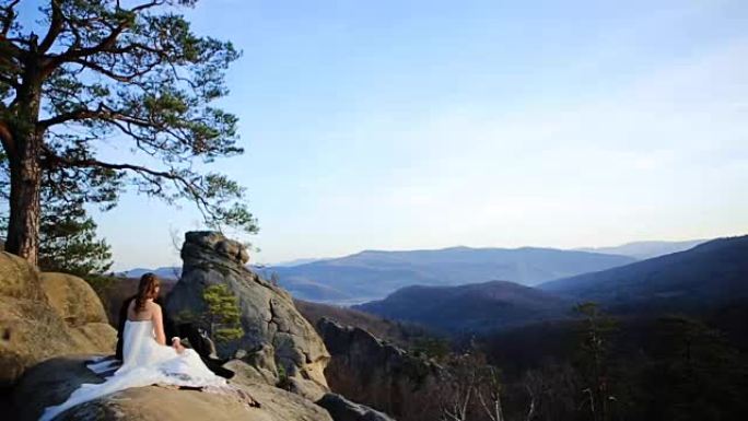 美丽神话般的快乐新娘和时尚的新郎坐在阳光明媚的迷人山脉的背景上