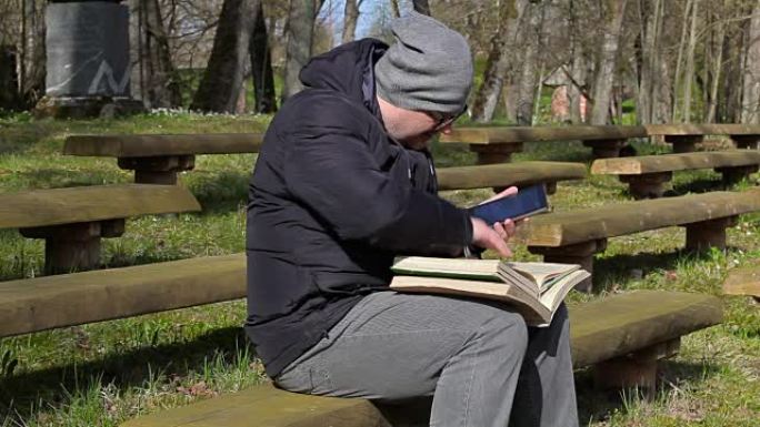 在公园的长凳上使用平板电脑和看书的人