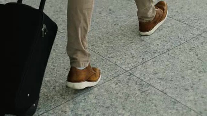 将行李步行到机场航站楼的人腿特写镜头。