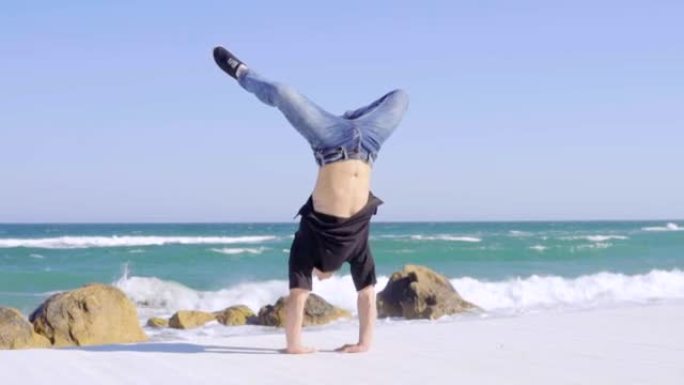 年轻强壮的男人表现出令人印象深刻的力量，在海滩上倒立。运动员训练执行倒立。在海滩上锻炼。慢动作镜头