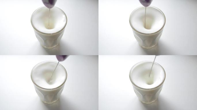 咖啡师用手奶泡将牛奶泡沫搅打在多面玻璃烧杯中。
