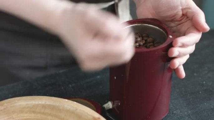 围裙中的女人将咖啡豆倒入研磨机中
