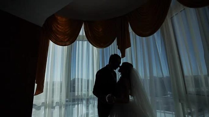 快乐的奢华新娘和新郎站在富裕房间的窗灯前