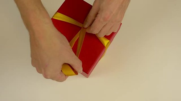 快速运动时间流逝。包装红色礼品盒。高加索人手包装礼品盒。男人的手在红色纸板箱上系上丝带。俯视图特写。