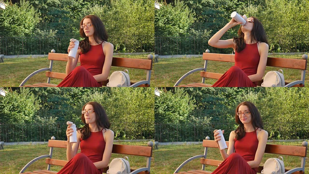 穿着深红色长裙和眼镜的可爱女性坐在户外的长椅上，喝着温热杯里的东西，露出大手指。
