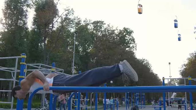 运动男子在城市公园运动场的双杠上俯卧撑。强壮的年轻肌肉发达的家伙在夏天户外训练。运动员在操场上锻炼。