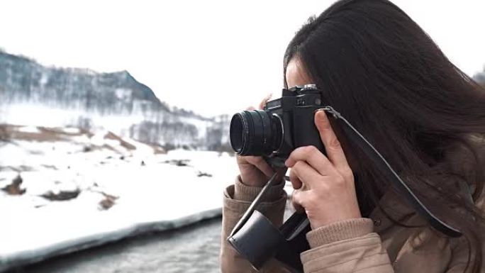十几岁的女孩在冬天的背景下拍照，用一台旧的电影相机拍摄群山。手持镜头