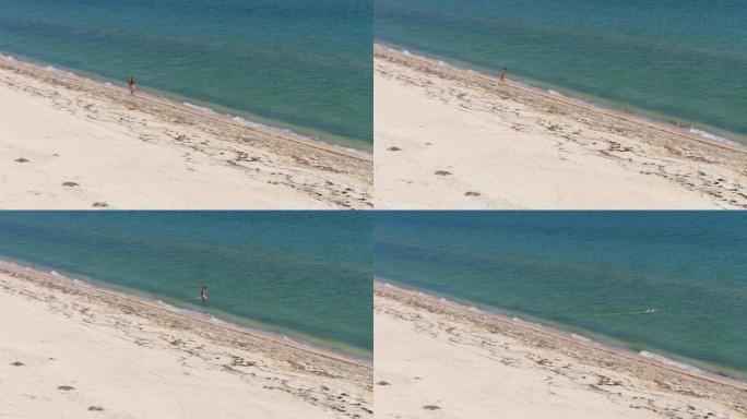 一个男人在荒芜的海滩上，在海里散步和游泳