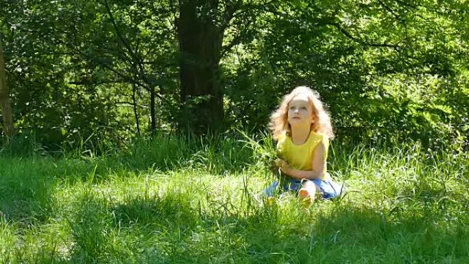 顽皮的小女孩在阳光明媚的日子里在公园里享受温暖的夏日天气。女孩子捡起绿草，看着镜头。