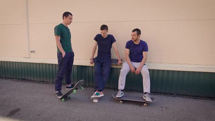 三个朋友青少年享受户外运动的乐趣，在滑板公园微笑和聊天。积极的年轻人表现出健康的生活方式，在街上度过