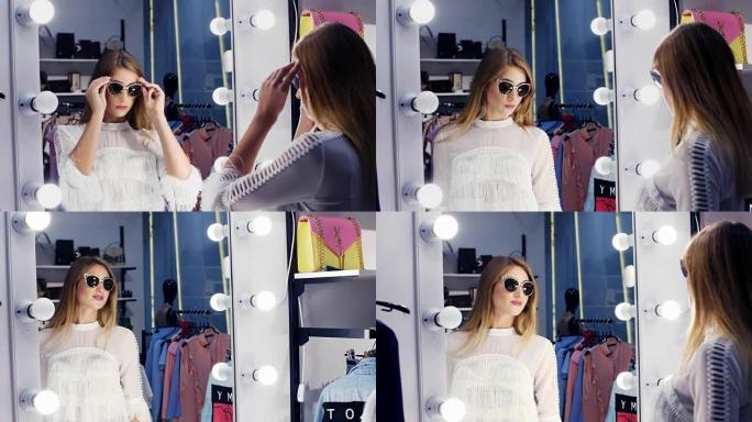 性感的女孩，高个子，美丽的金发女人在一家时尚的商店里试戴太阳镜，精品店，在镜子前欣赏自己，微笑着。慢