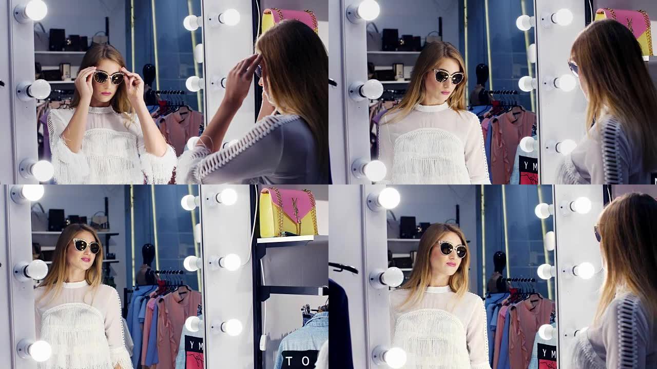 性感的女孩，高个子，美丽的金发女人在一家时尚的商店里试戴太阳镜，精品店，在镜子前欣赏自己，微笑着。慢