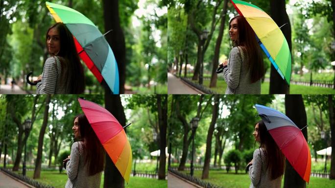 在城市公园的雨天，一个迷人的女人在旋转五颜六色的雨伞的后景