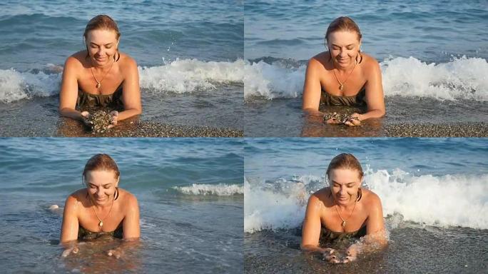 年轻女子躺在整理海水的海滩上，在slo-mo中选择贝壳