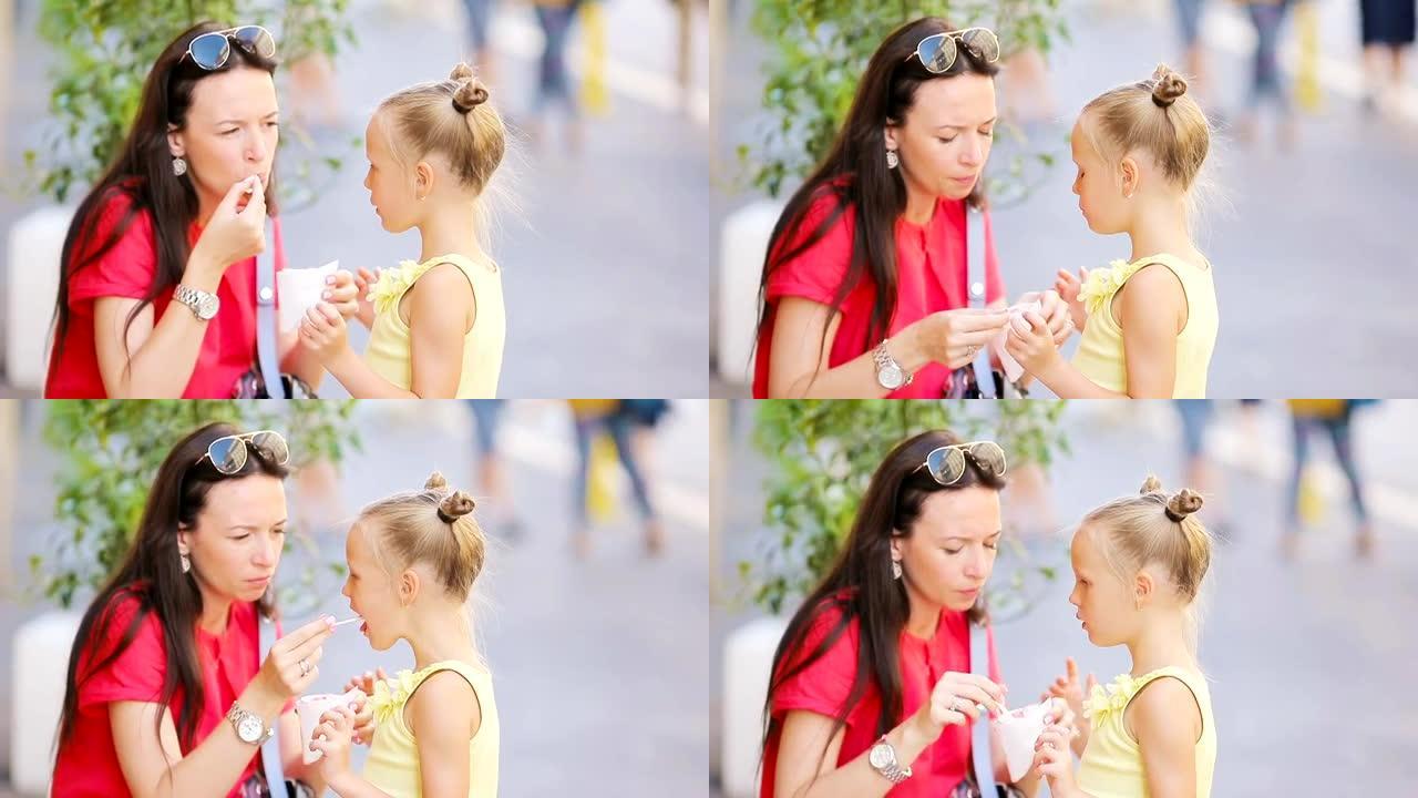 年轻的母亲和女儿在户外吃冰淇淋。妈妈在街上喂他的女儿冰淇淋
