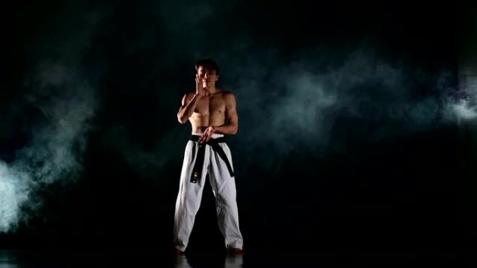 男子在黑色场地上训练跆拳道或空手道。慢动作