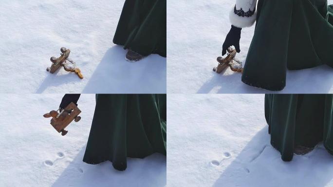 儿童玩具躺在雪地里，女人拿着它。雪地里的小雪人玩具。手拿圣诞玩具复古七彩盒冬雪。白色袋子上的复古东西