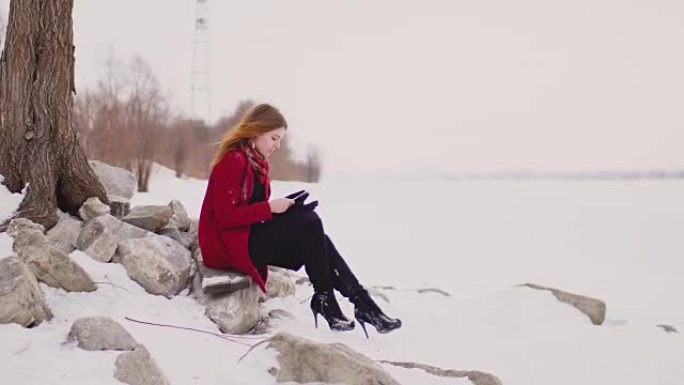 女人文本浏览在线智能手机在冬季森林，在田野里下雪的天气