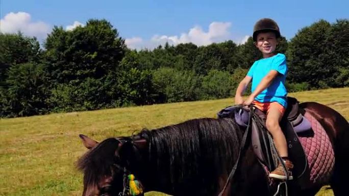 戴着头盔的快乐男孩在山上骑着棕色的马