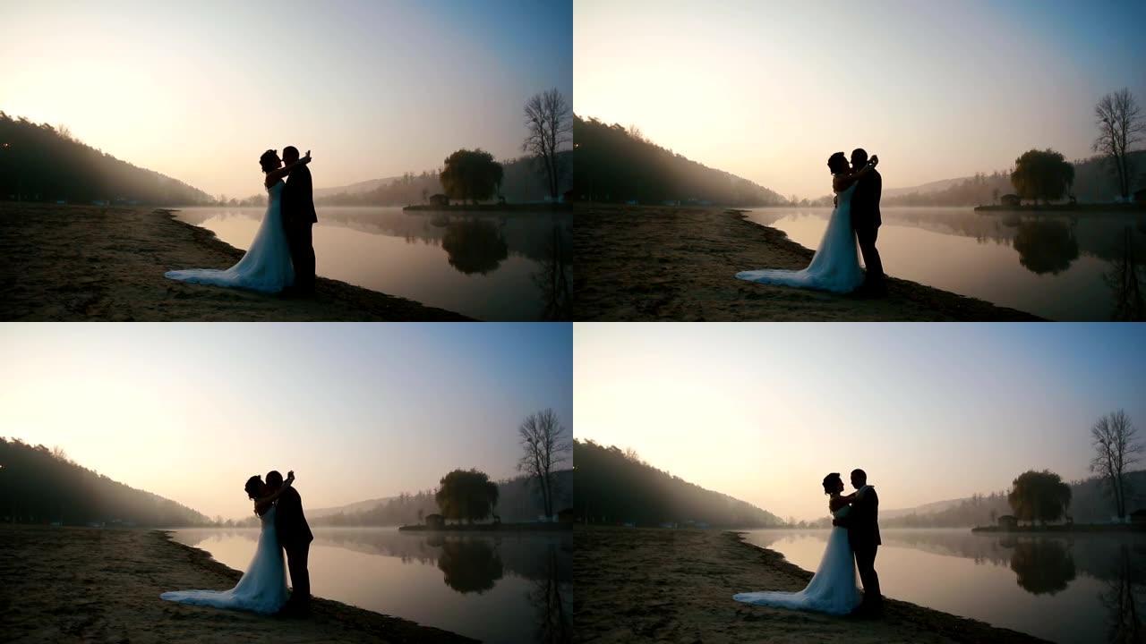 两对幸福的新婚夫妇在婚礼当天的傍晚在日落的浪漫湖上进行甜言蜜语和接吻