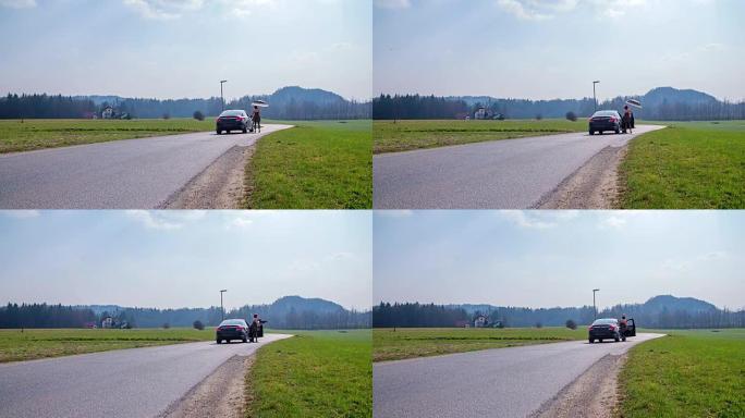 在一个阳光明媚的日子里，女人在乡村道路中间进入汽车，在与男人交谈后，镜头处于慢动作状态。