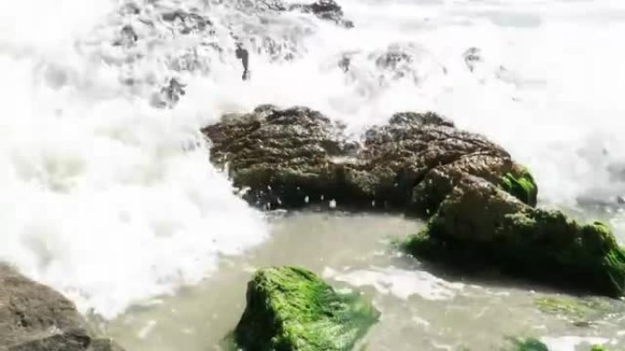 岸上的天然花岗岩岩层，其中一些覆盖着水生植被，被泡沫状的海浪重击，在缓慢运动中